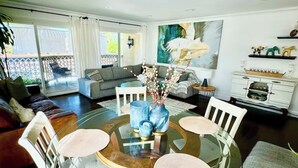 Ein modernes Wohnzimmer mit einem Glastisch, umgeben von weißen Stühlen, einem grauen Sofa und einem großen Gemälde an der Wand.