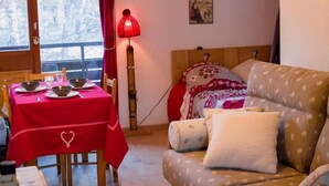 Een gezellige kamer met een eettafel gedekt voor twee personen, een bed met bloemenbeddengoed en een rode lamp.