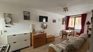 Een knus woongedeelte met een kitchenette, een bank, een eettafel en een aan de muur bevestigde televisie.