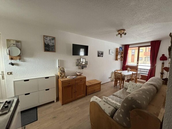 Een knus woongedeelte met een kitchenette, een bank, een eettafel en een aan de muur bevestigde televisie.