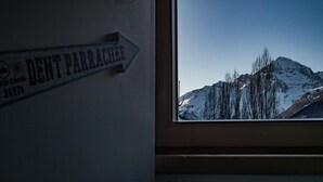Een raam met uitzicht op besneeuwde bergen en een bord met de tekst 'Dent Parrachee'.