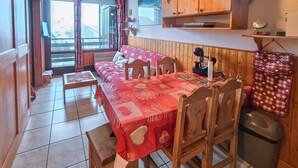 Un coin repas accueillant avec une table et des chaises en bois, une nappe rouge et une vue sur l’extérieur grâce à de grandes fenêtres.