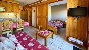 Une pièce confortable, dotée de meubles en bois, d’une télévision et d’une petite cuisine.