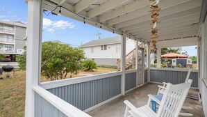 A covered porch with white chairs, a view of a residential area, and a sign indicating a craft beer tap. - Low Tide at Coral Reef  2 BDRM  1.5 bath Sleeps 5 with Linens Included! (Carolina Beach)