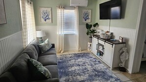 A living room with a sofa, a blue rug, a TV, and a cabinet. - Low Tide at Coral Reef  2 BDRM  1.5 bath Sleeps 5 with Linens Included! (Carolina Beach)