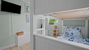 A bunk bed with a blue and white nautical-themed bedspread, a television mounted on the wall, and a small window with a view of greenery. - Low Tide at Coral Reef  2 BDRM  1.5 bath Sleeps 5 with Linens Included! (Carolina Beach)