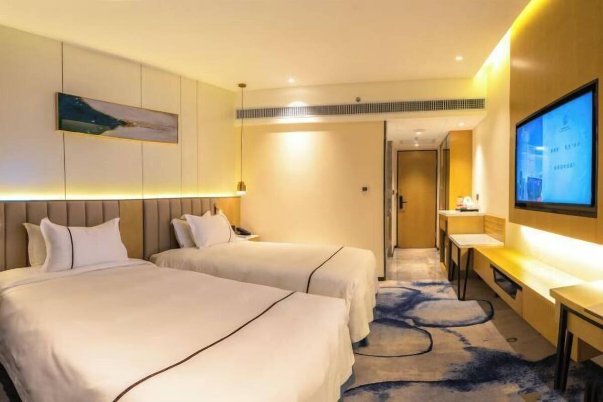 A hotel room with two beds, a TV, a desk, and a painting on the wall.