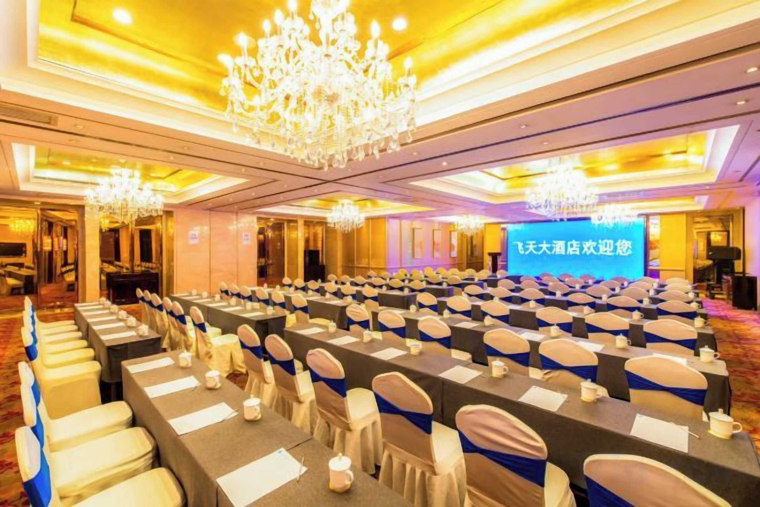 A conference room with rows of tables and chairs, a large screen, and chandeliers.