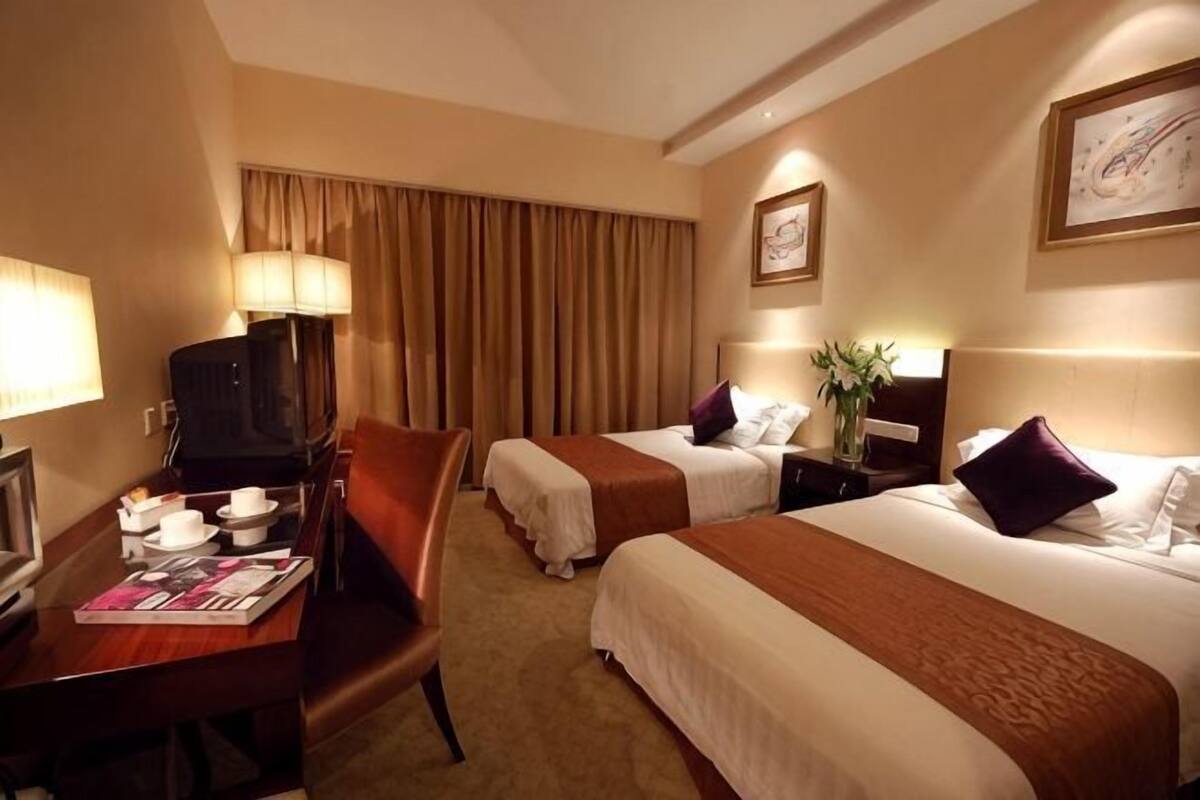 A hotel room with two beds, a desk with a TV, and a chair.