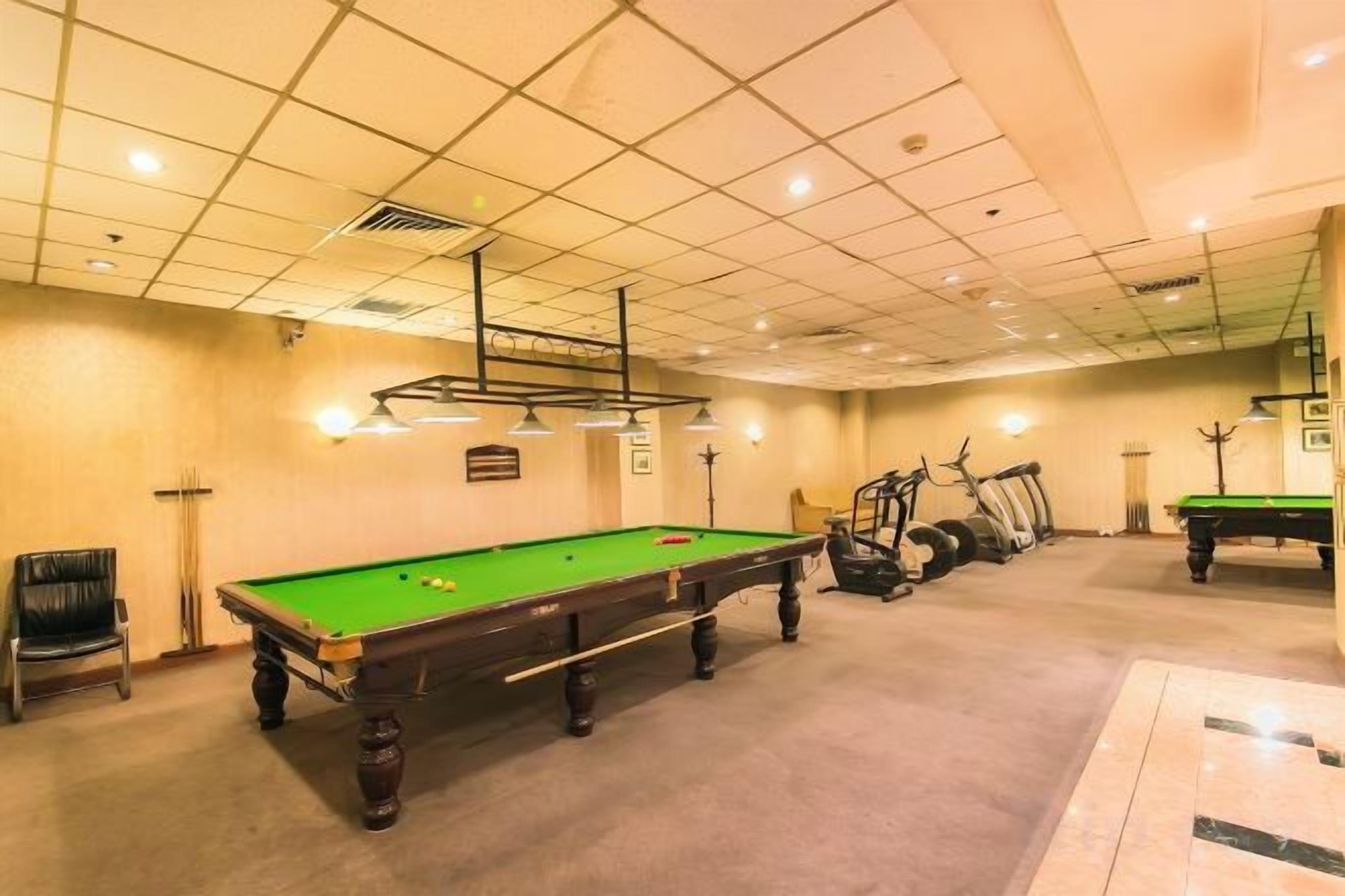 A pool table with a green felt surface, a seating area with a chair, and a wall-mounted clock.