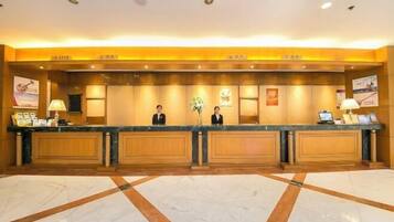 A hotel reception area with a marble floor, wooden reception desk, and a receptionist.