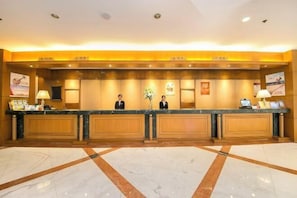 A hotel reception area with a marble floor, wooden reception desk, and a receptionist. - Lanzhou Legend Hotel (Lanzhou Railway Station & Lanzhou University Subway Station) (Lanzhou)