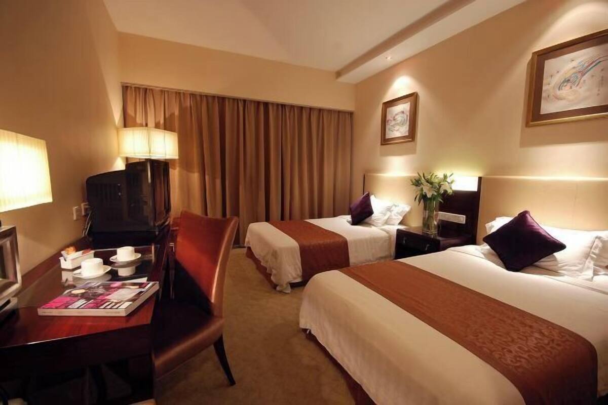 A hotel room with two beds, a desk with a coffee maker, a TV, and a window with curtains.