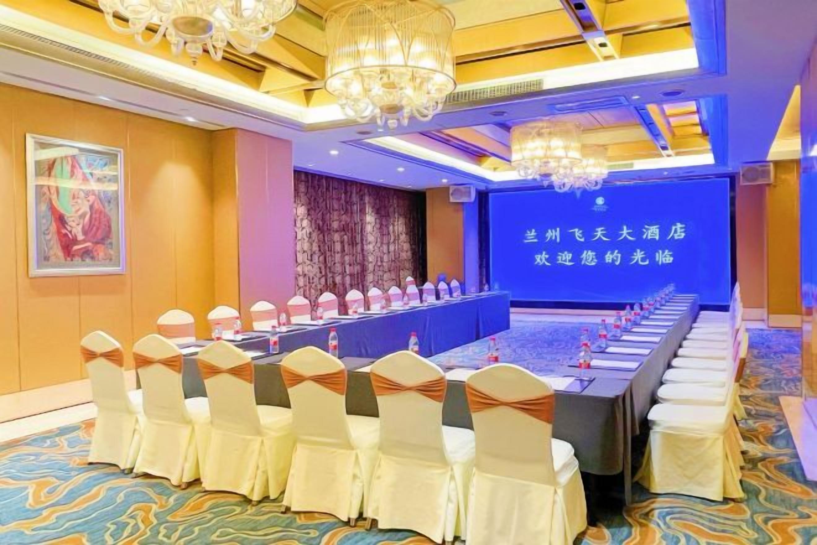 A conference room with a long table, chairs with white covers, and a blue screen with Chinese text.