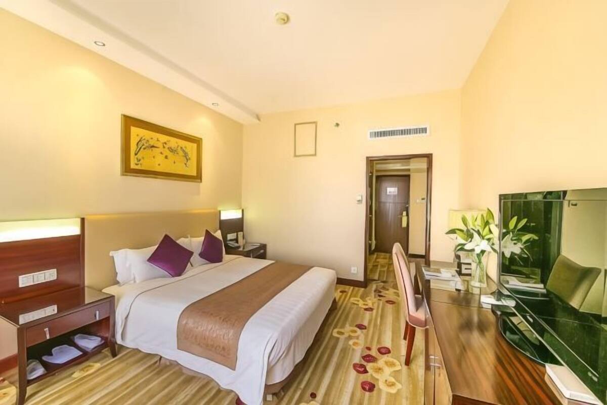 A hotel room with a bed, bedside tables, a TV, and a door leading to another room.