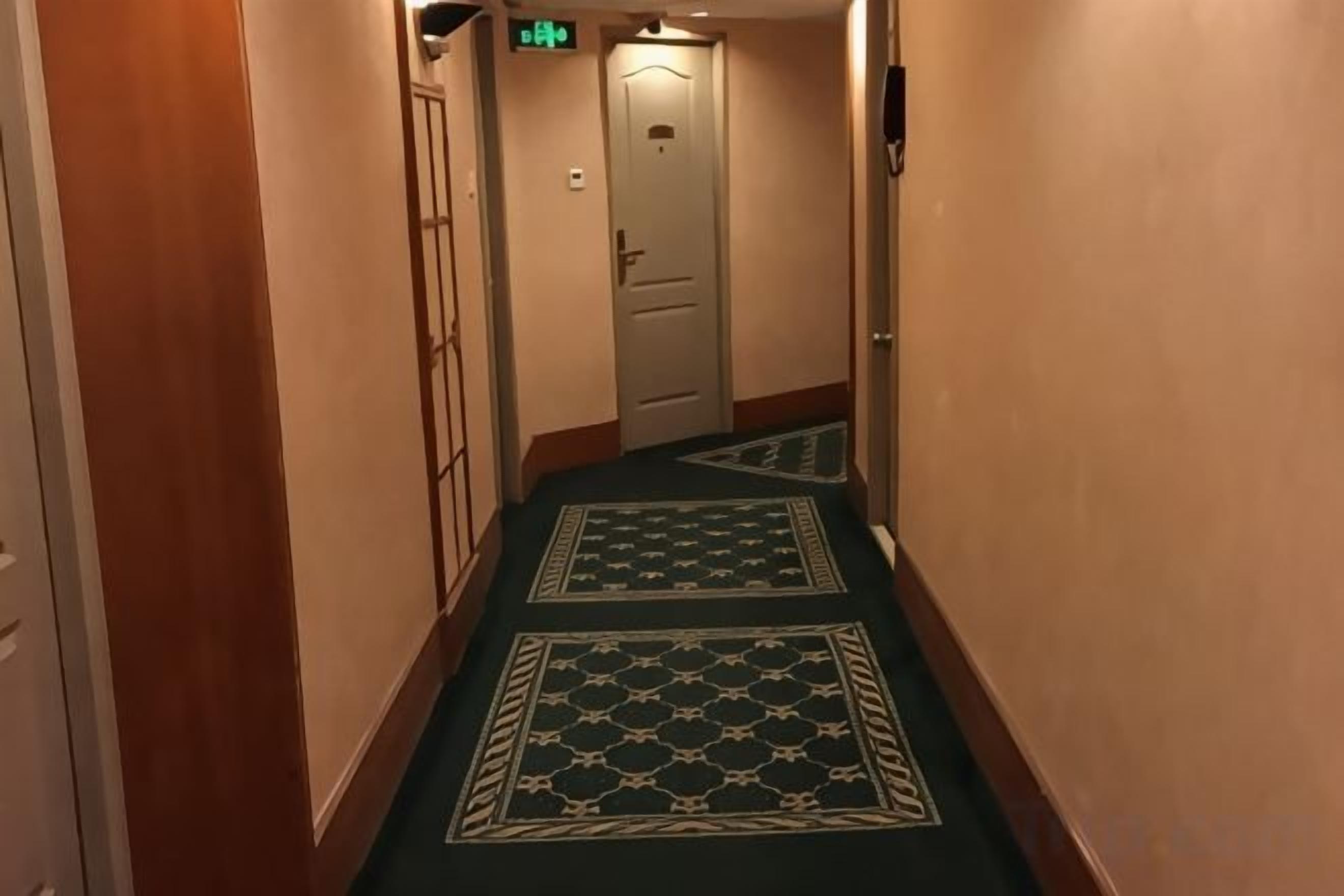 En gang med tæppe med mønster og trævægge, der fører hen til en dør med et skilt over.