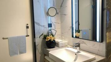 Een moderne badkamer met een marmeren wand, een wit wastafelmeubel, een ronde spiegel en een handdoekhouder.