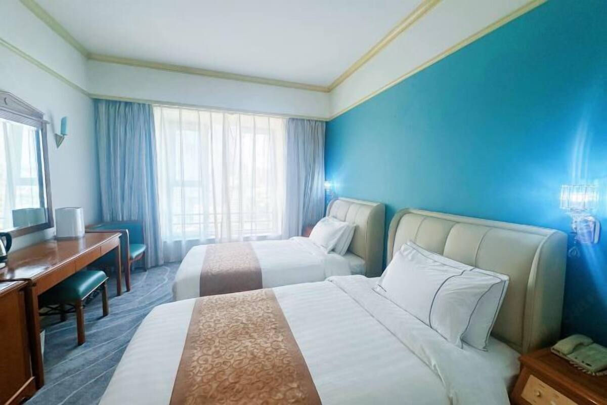 A hotel room with two beds, a desk, a chair, a TV, and a nightstand.