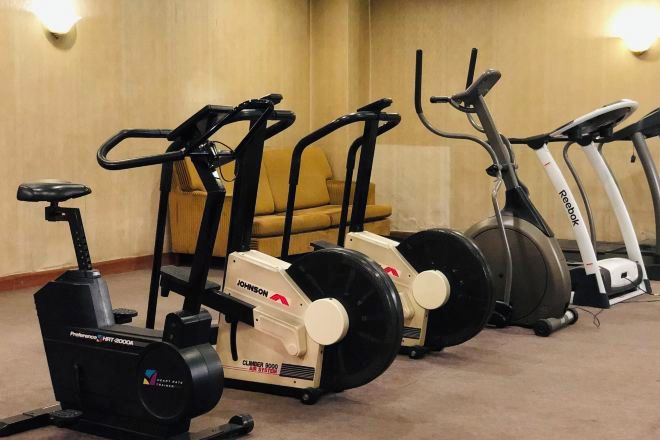 A row of stationary bikes in a room with a beige carpet and a yellow chair in the background.