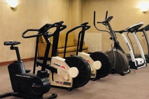 A row of stationary bikes in a room with a beige carpet and a yellow chair in the background. - Lanzhou Legend Hotel (Lanzhou Railway Station & Lanzhou University Subway Station) (Lanzhou)