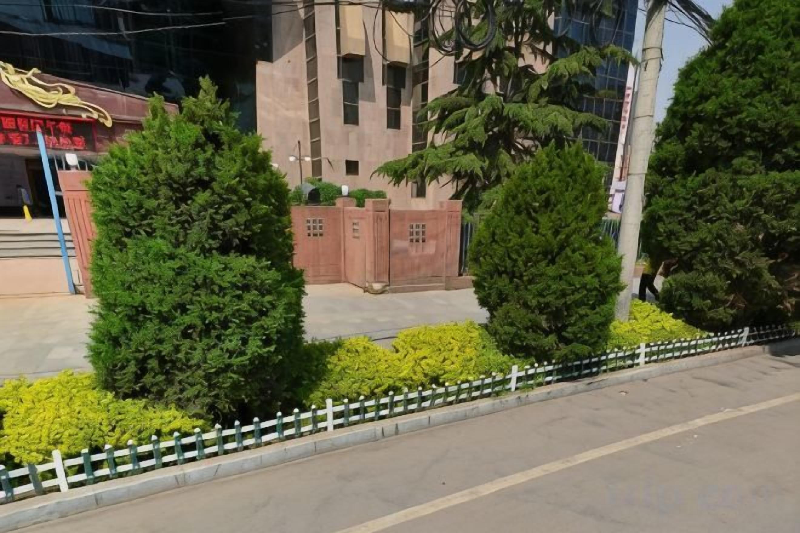 Un edificio con un portón de entrada rojo, rodeado de árboles y arbustos verdes.