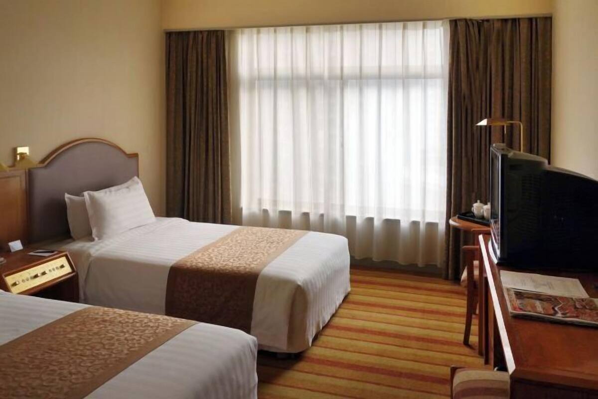 A hotel room with two beds, a television, a desk, and a large window with curtains.
