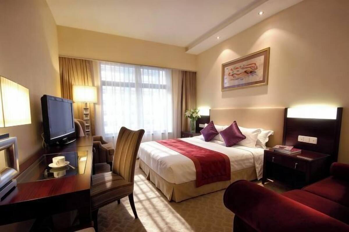 A hotel room with a bed, a desk with a computer, a chair, a TV, and a nightstand.