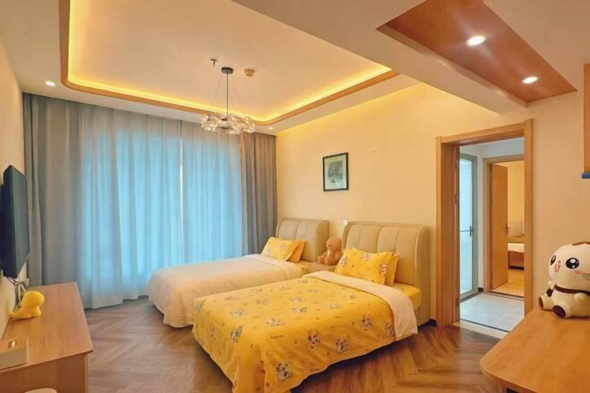 A hotel room with two beds, a desk, a television, and a large window with curtains.