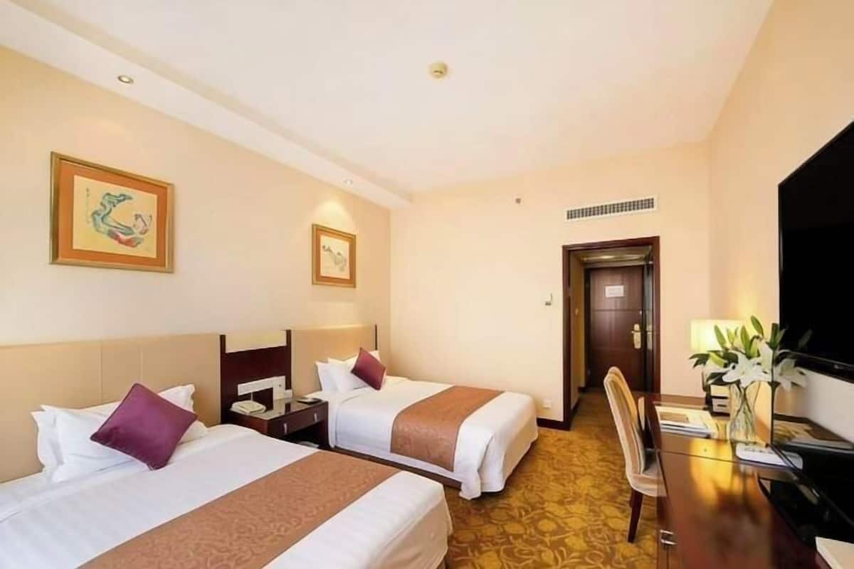 A hotel room with two beds, a desk with a chair, a television, and a door.
