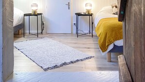 Un dormitori d'altell acollidor amb sostre inclinat, dues taules de nit amb làmpades, un llit amb llençol groc i una porta blanca.