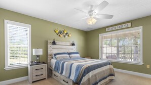 Un dormitorio con cama, mesita de noche, lámpara, ventilador de techo y ventana con persianas.