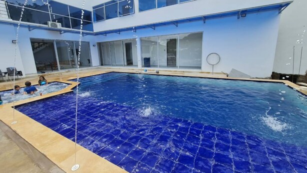 A swimming pool with a blue tiled floor, surrounded by a building with large windows and a glass door.