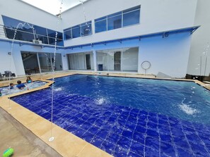 A swimming pool with a blue tiled floor, surrounded by a building with large windows and a glass door.