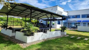 A modern outdoor patio area with a covered seating area, surrounded by planters and a well-maintained lawn.