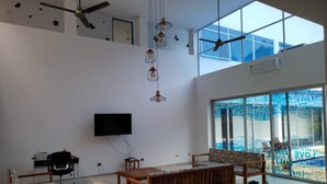 A spacious living area with a large window, ceiling fans, a flat-screen TV, and a wooden bench.