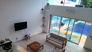 A living room with a TV, wooden furniture, and a view of a pool through large glass doors.
