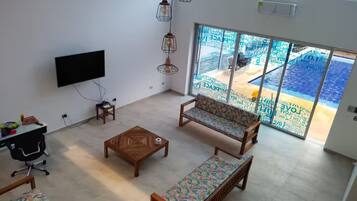 A living room with a TV, wooden furniture, and a view of a pool through large glass doors.