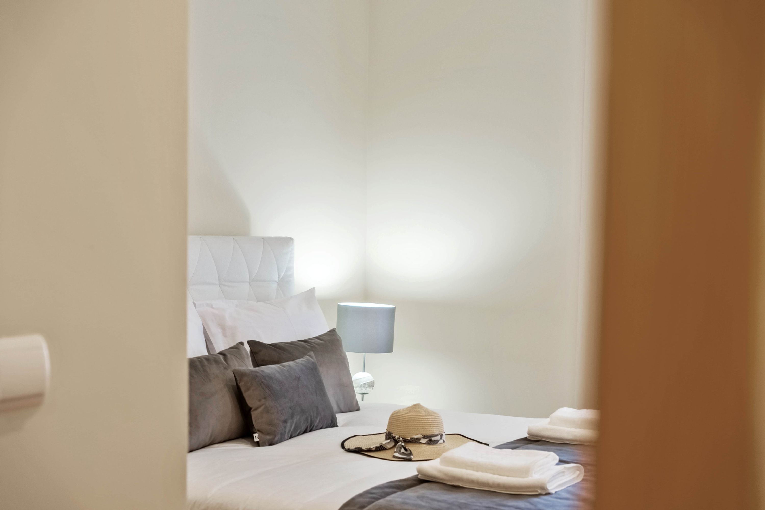 A neatly made bed with pillows, a lamp, and a hat on the bed.