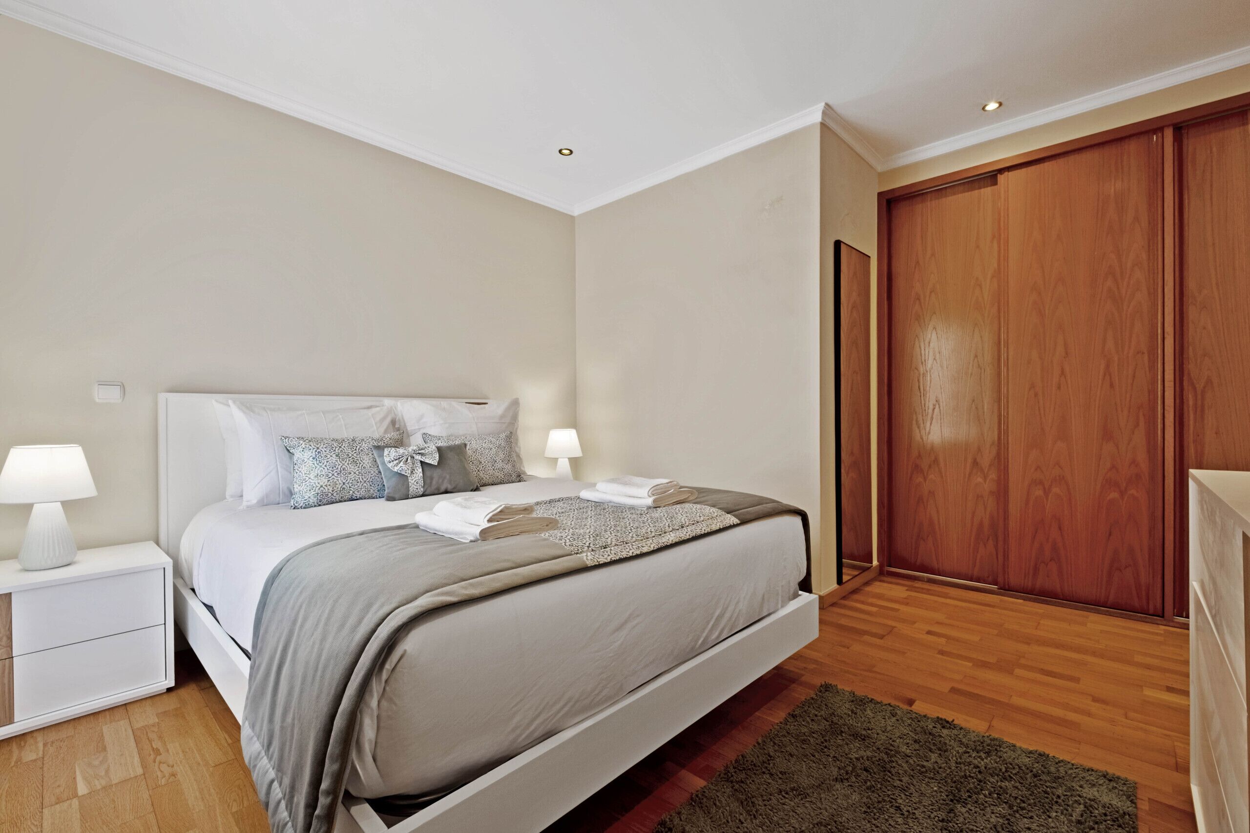 Une chambre à coucher avec un lit, des tables de chevet, une armoire en bois et un tapis.
