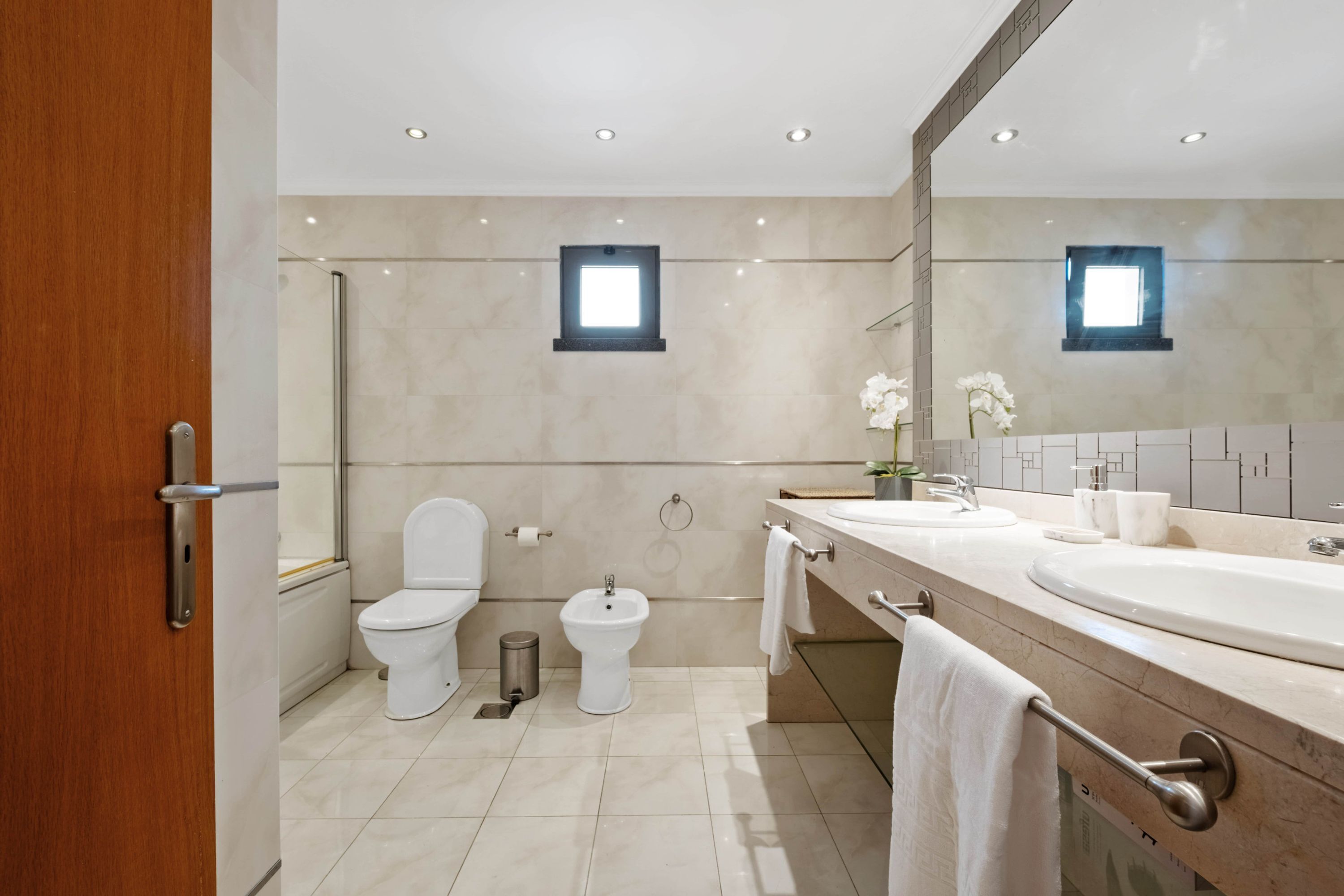 A modern bathroom with two sinks, a toilet, bidet, and a mirror.