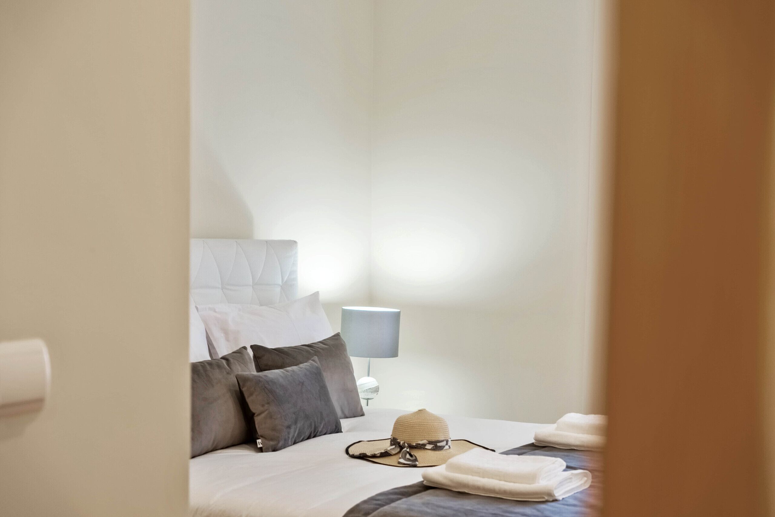 A neatly made bed with pillows, a hat, and folded towels.