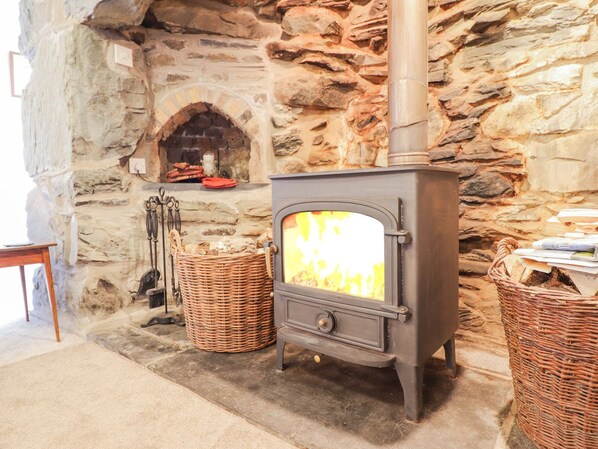 Una chimenea de piedra con estufa de leña, cestas de mimbre y pared de piedra.