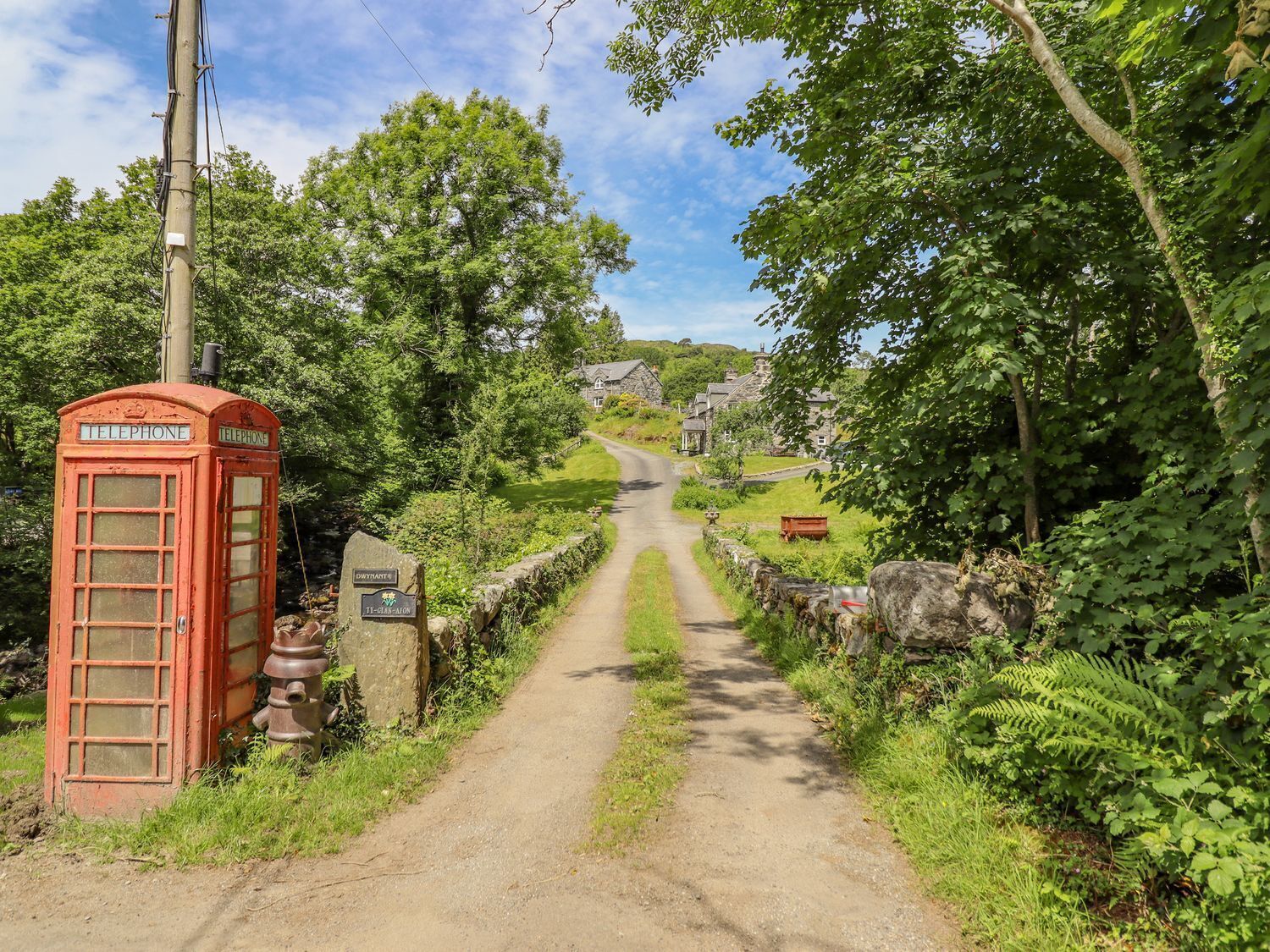 A rural road leading to a village with a traditional red telephone booth on the left.