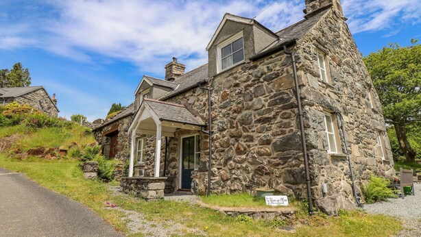 A stone house with a porch, a chimney, and a sign in front. - Ty Glan Yr Afon (Dolgellau)