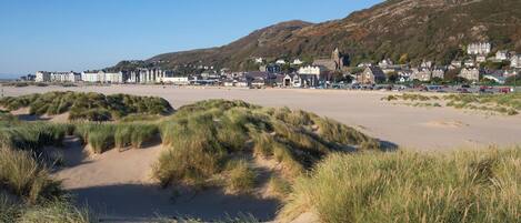 A coastal town with a sandy beach, dunes, and buildings in the background.