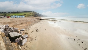 A beach with pebbles, a rocky breakwater, and a row of blue beach huts. - Ty Glan Yr Afon (Dolgellau)