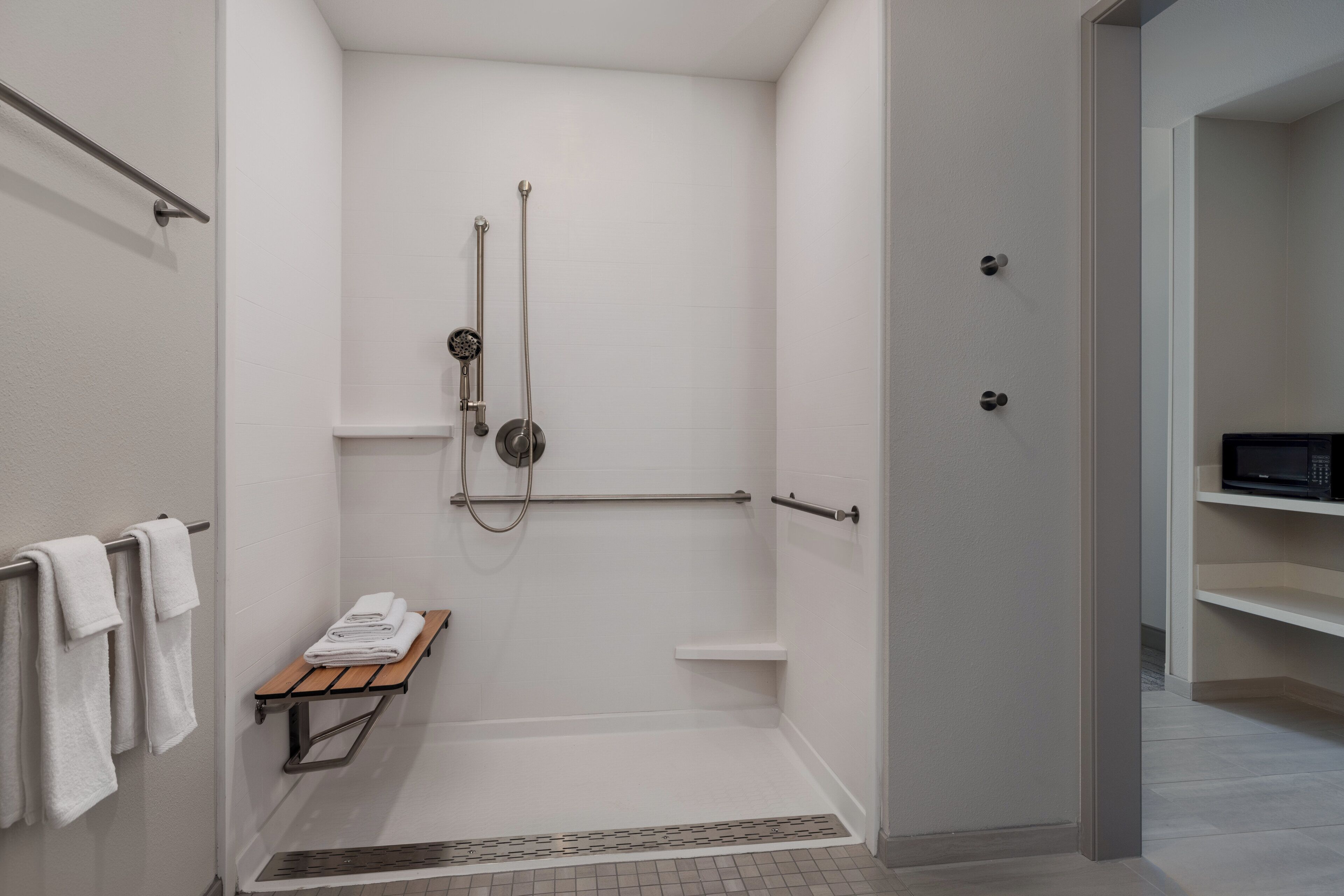 Een moderne badkamer met een douche, een handdoekhouder en een magnetron op een plank.