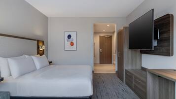 A modern hotel room with a large bed, a flat-screen TV mounted on the wall, a wooden cabinet, and a framed artwork on the wall.