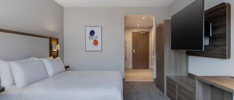A modern hotel room with a large bed, a flat-screen TV mounted on the wall, a wooden cabinet, and a framed artwork on the wall.