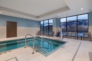 Una piscina interior con agua azul cristalina, una puerta de madera y grandes ventanales con vistas a las montañas.